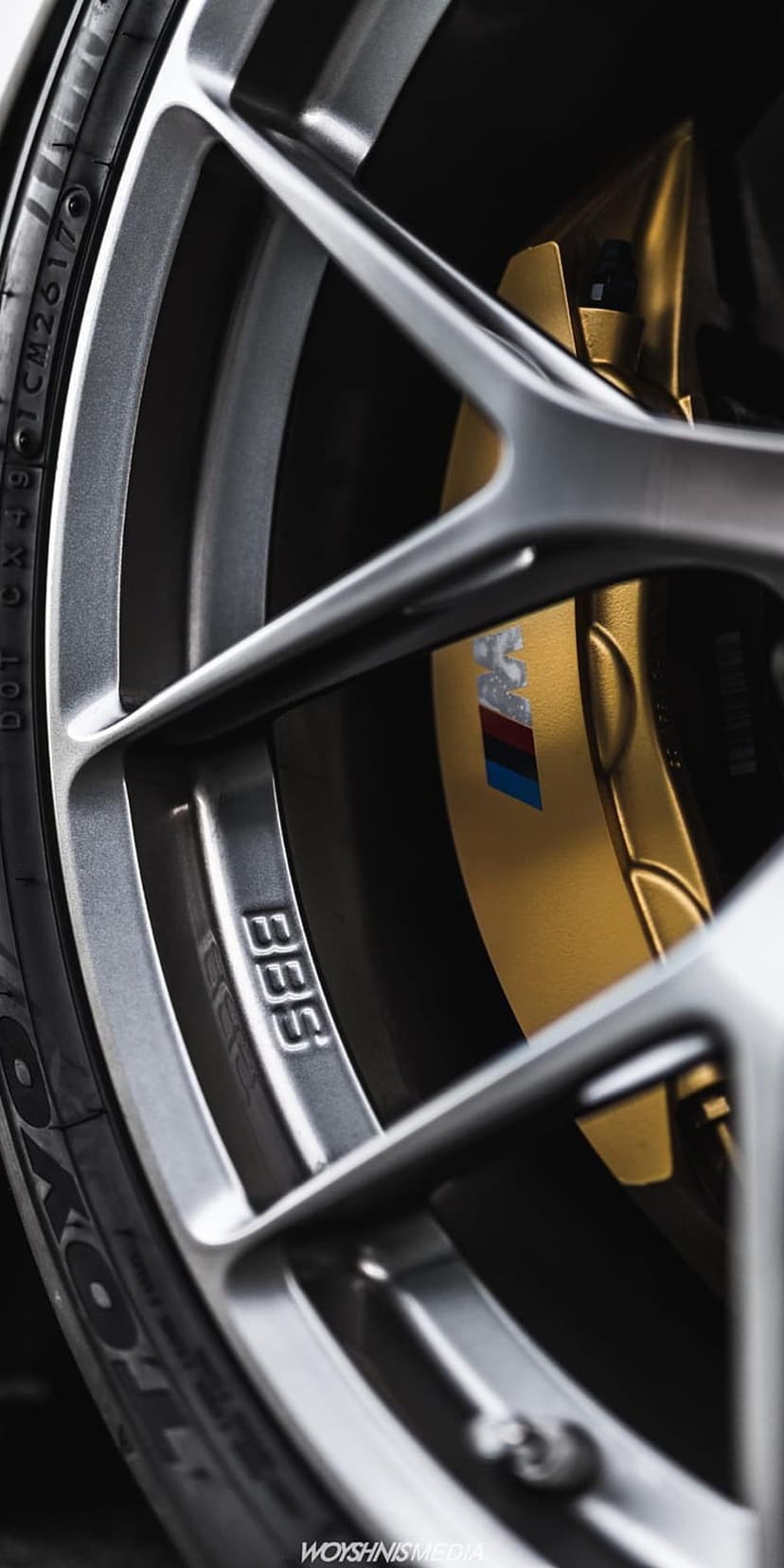 Gold M Sport brake caliper and silver BBS rim with a tri-color emblem shown in a detailed macro composition.