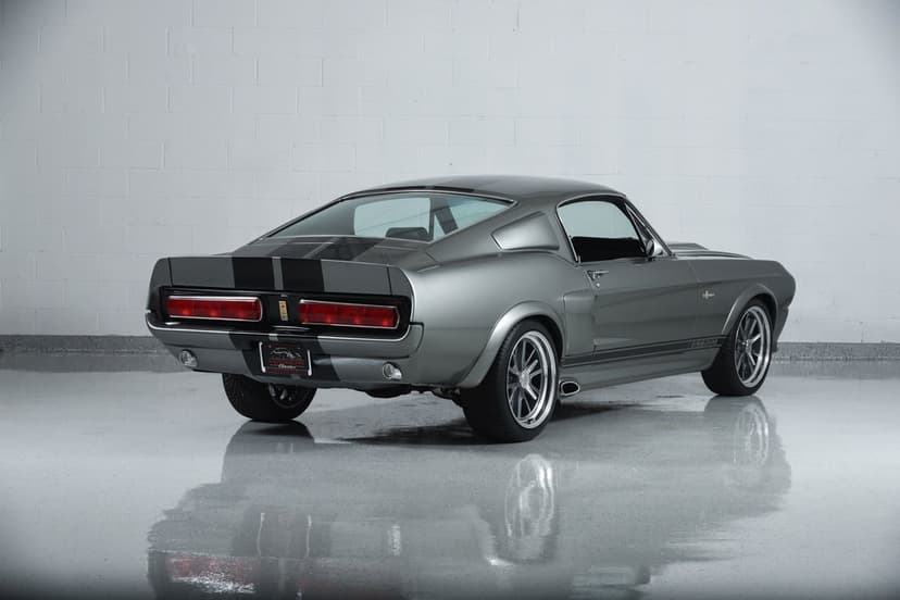 Grey 1967 Shelby Mustang GT500 with black racing stripes in a white studio with a reflective floor.