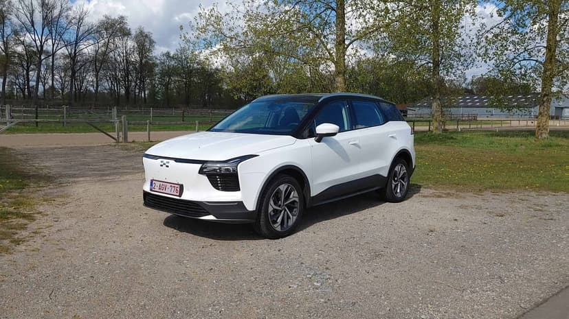 White Aiways U5 electric SUV parked on a gravel path surrounded by green trees and a wooden fence under a blue sky.