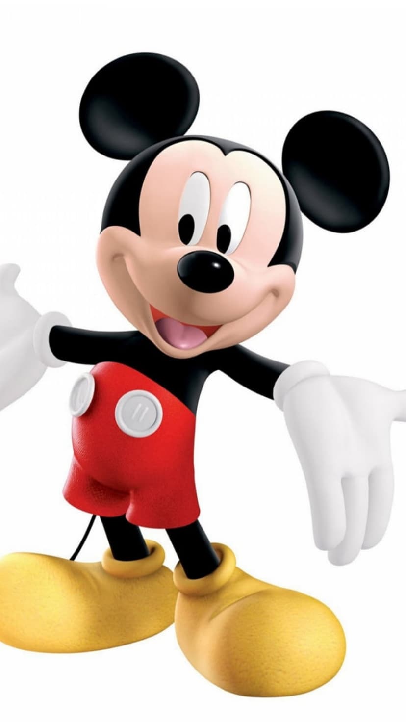 Mickey Mouse stands with open arms wearing white gloves, red shorts, and yellow shoes against a simple backdrop.