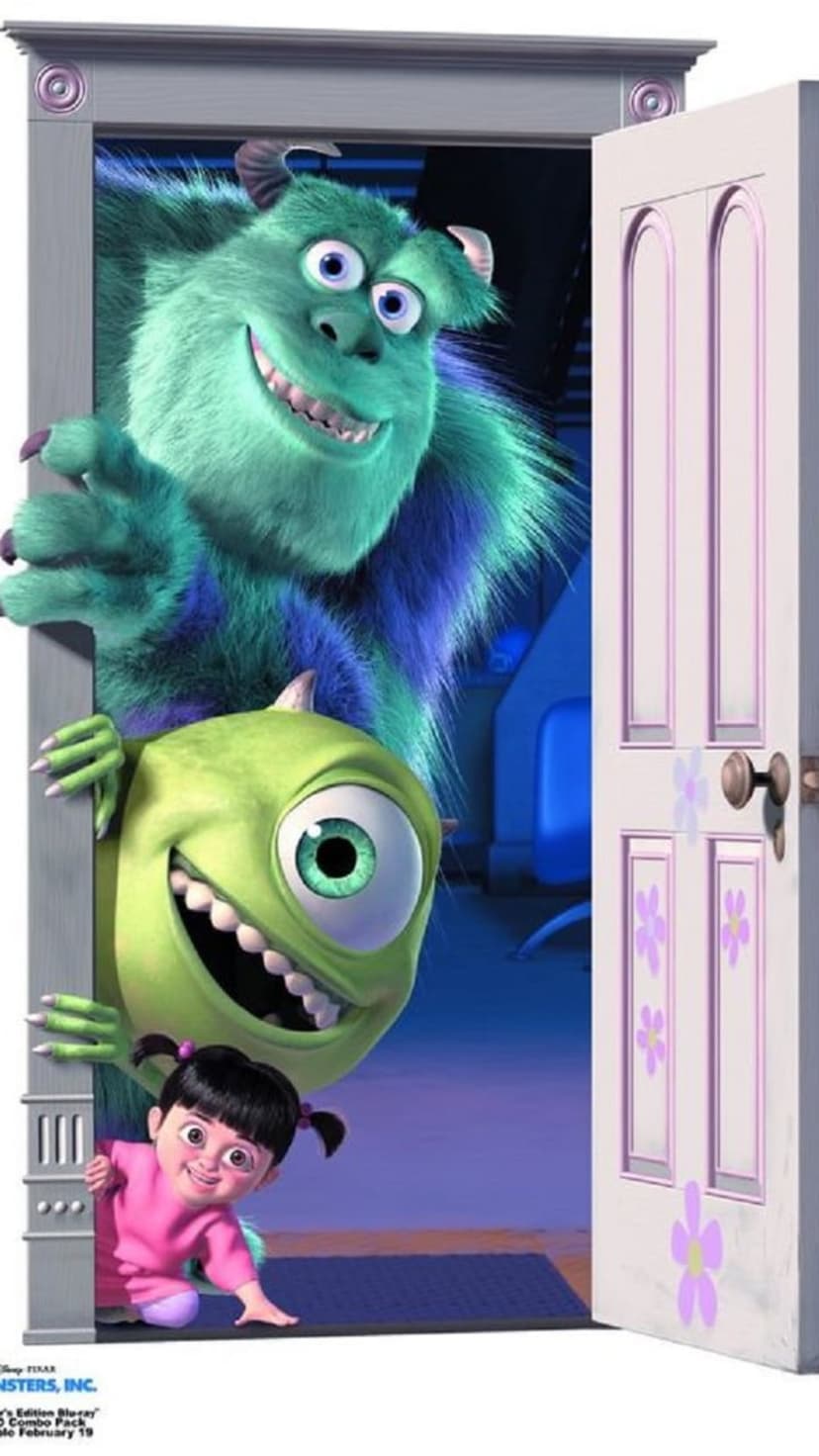 Sulley, Mike Wazowski, and Boo peek through an open white bedroom door with curious expressions on their faces.