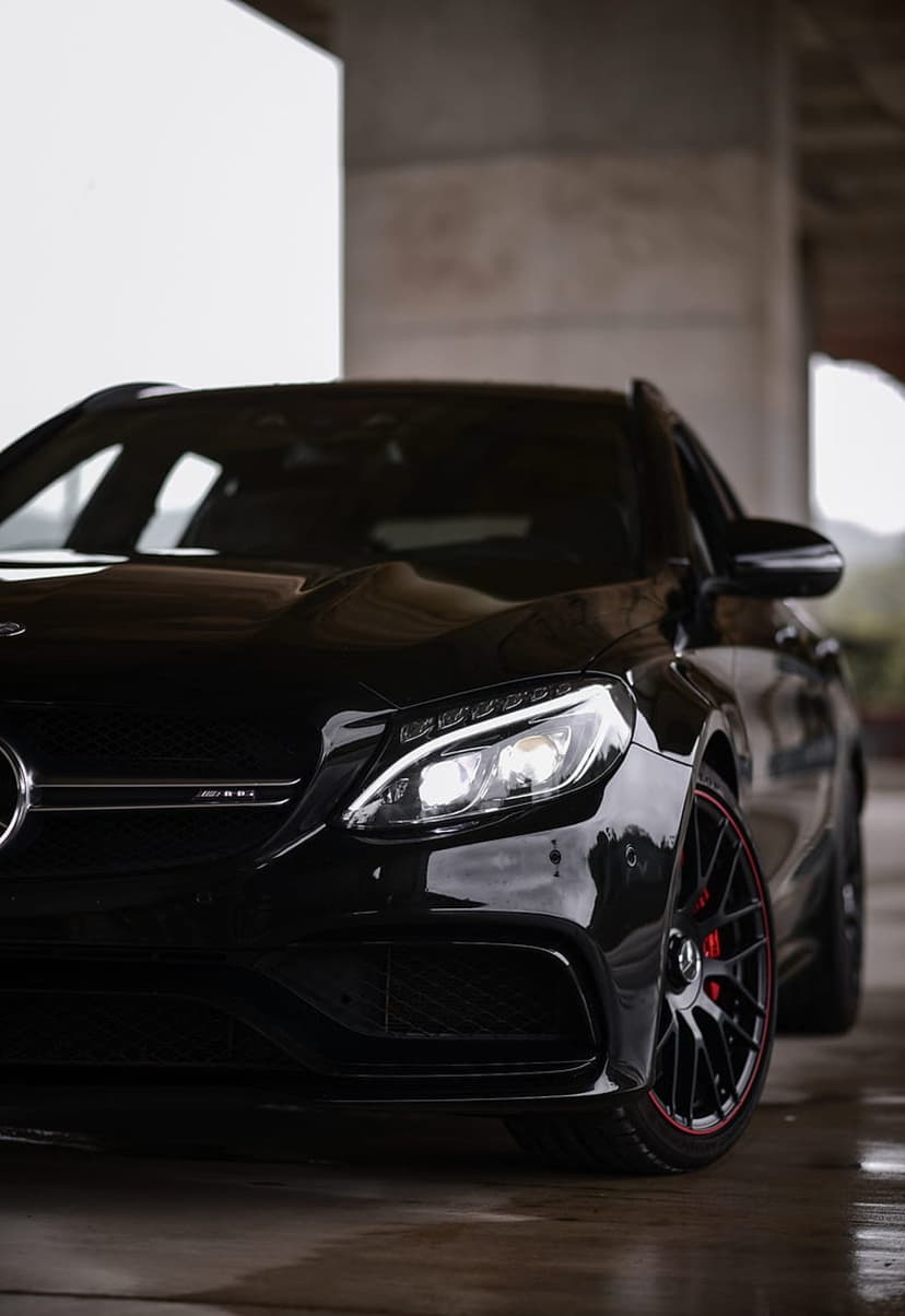 Black Mercedes-AMG estate car with LED headlights parked on wet pavement beneath a concrete structure.