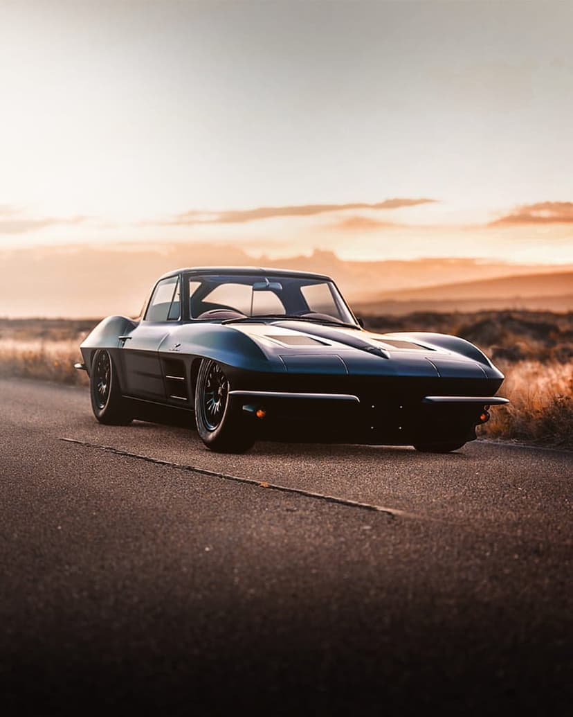 Blue Corvette Stingray on a desert road under an orange sunset sky with long shadows across the dry landscape.