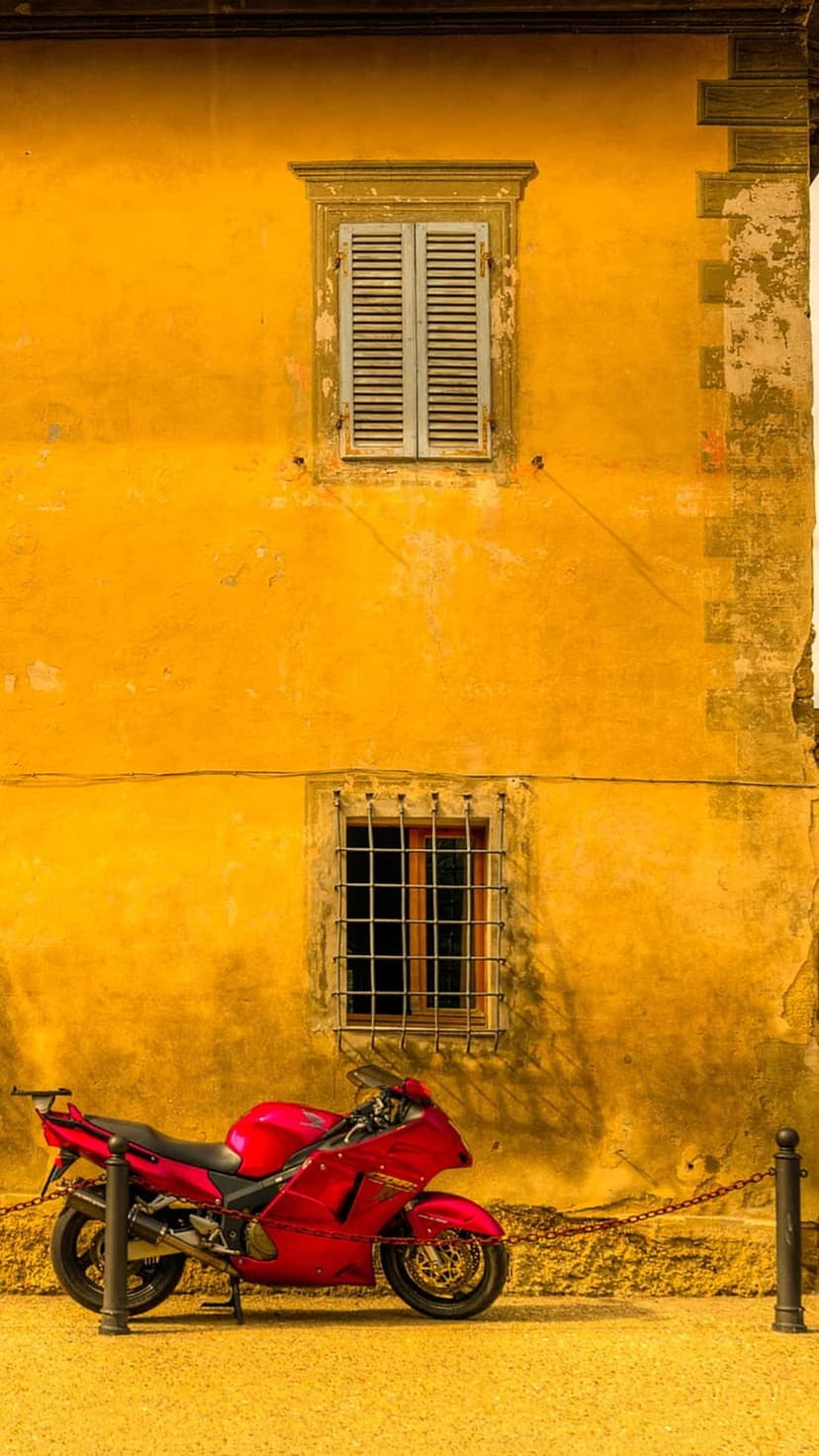 Red sport motorcycle parked beside a textured yellow stucco wall with wooden shutters and a metal window grate.