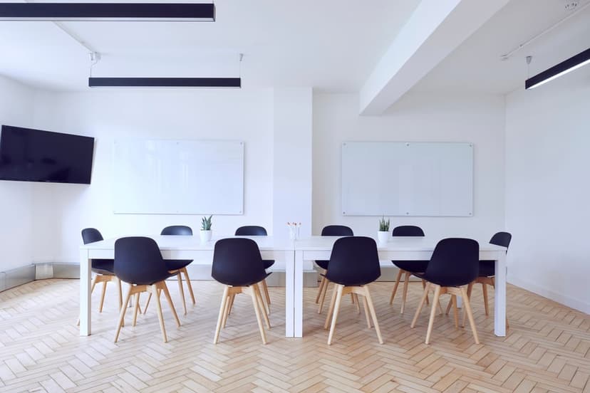 Sleek black office chairs surround a white table on light wood floors in a bright, modern meeting room.