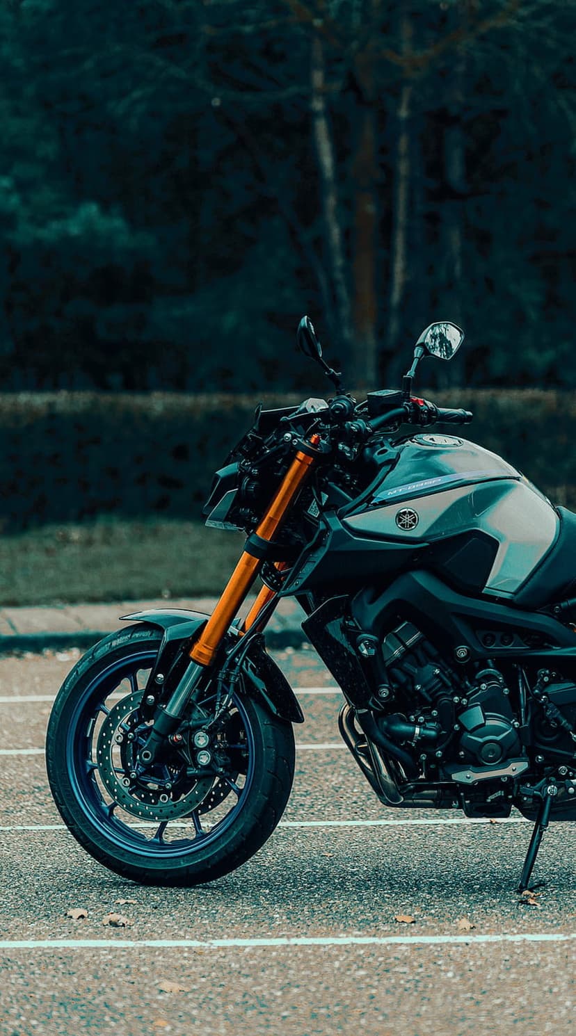 Yamaha motorcycle front wheel and orange forks on asphalt with a blurred forest background and dark tones.