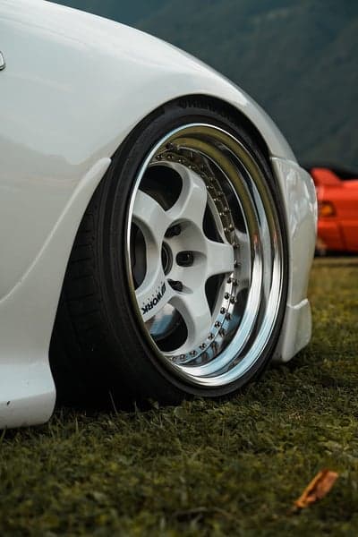 White car wheel and tire on grass with red car background
