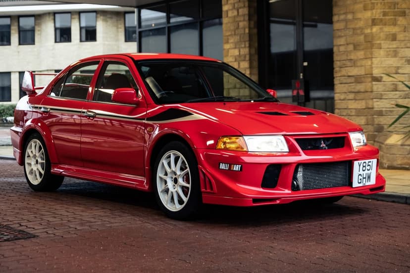Red Mitsubishi Lancer Evolution VI TME with white Ralliart decals and wheels parked on a brick courtyard.
