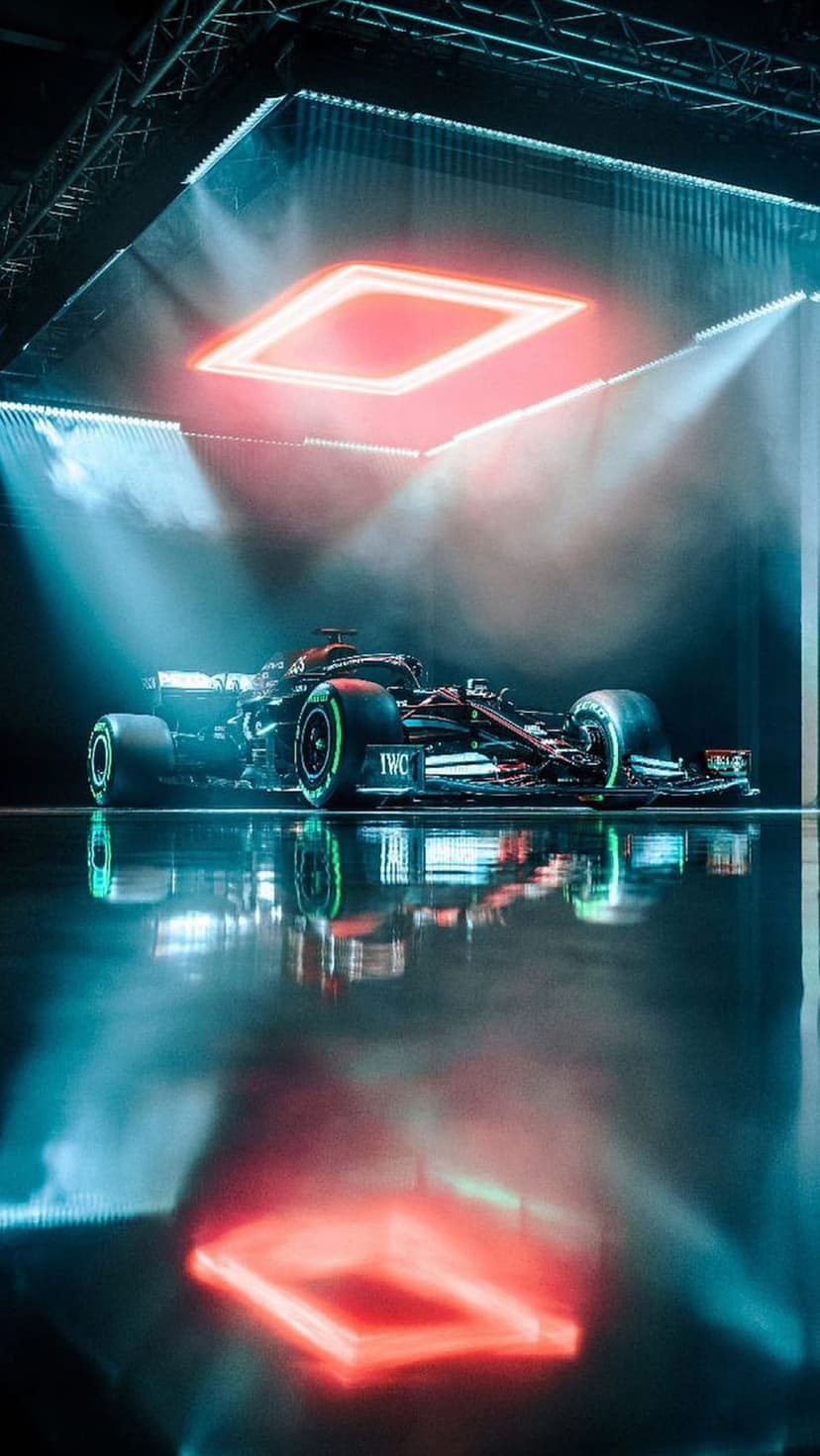 Formula 1 race car with green wheel accents reflecting on a floor amid red neon lights and dense smoke.
