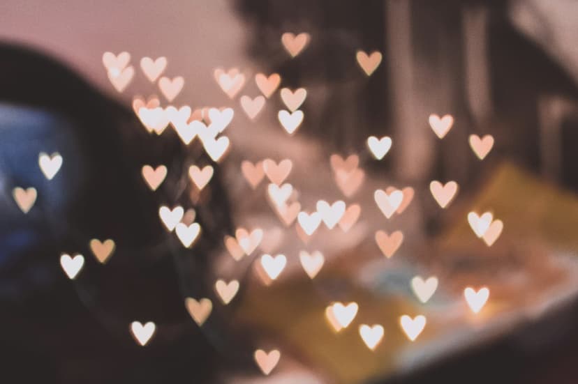Heart-shaped golden bokeh lights float in a soft-focus pattern with warm pink and orange glowing gradients.