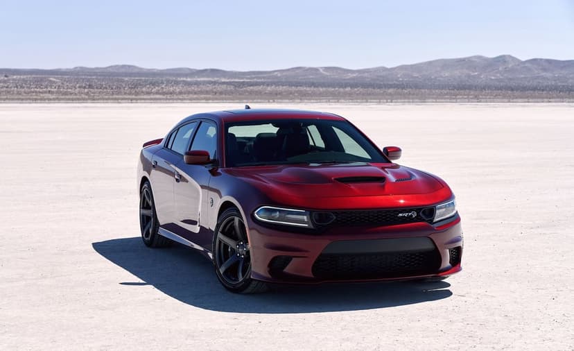 Red Dodge Charger SRT Hellcat parked on a white desert salt flat under a clear blue sky with distant mountains.