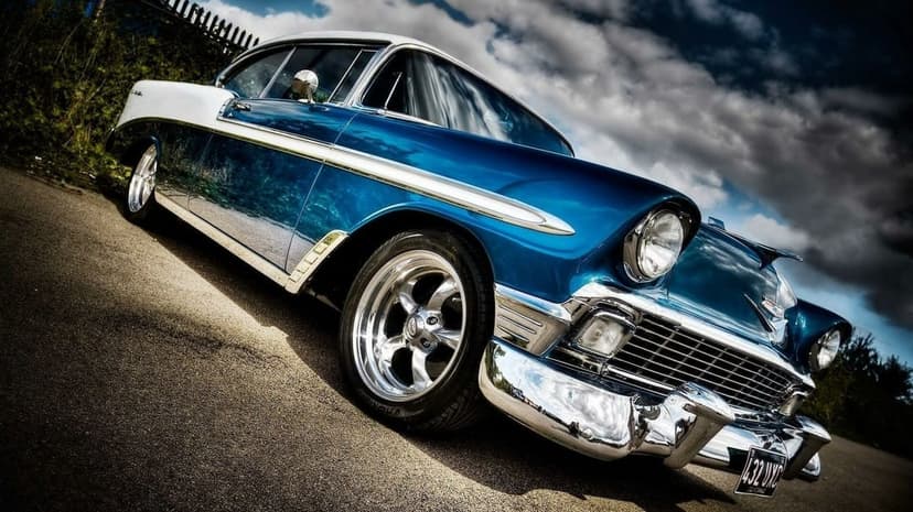 Two-tone blue and white 1956 Chevrolet with chrome accents parked under a moody, cloud-filled sky.