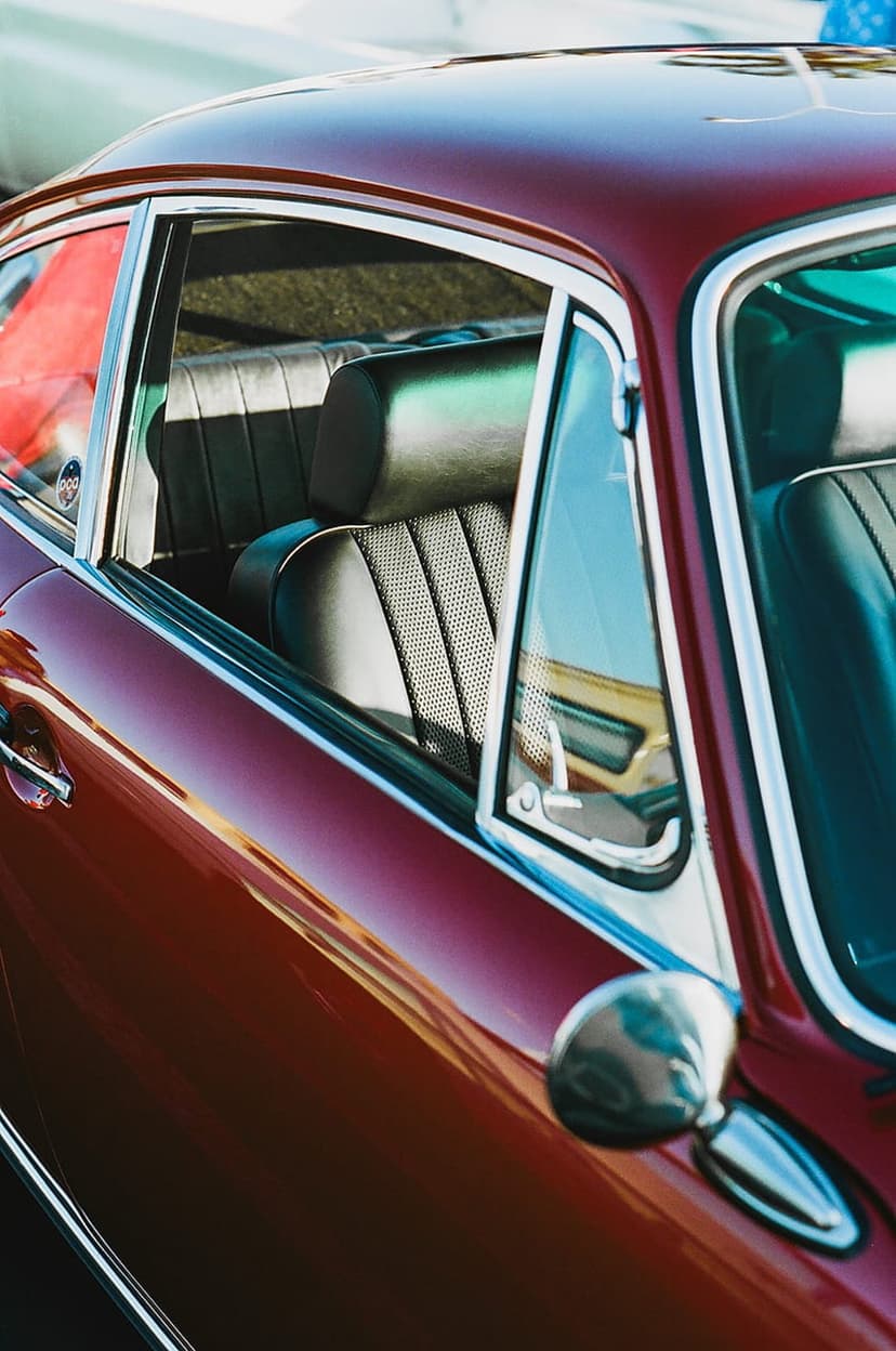 Burgundy perforated leather car seats with chrome trim and window reflections in a vintage Porsche interior.
