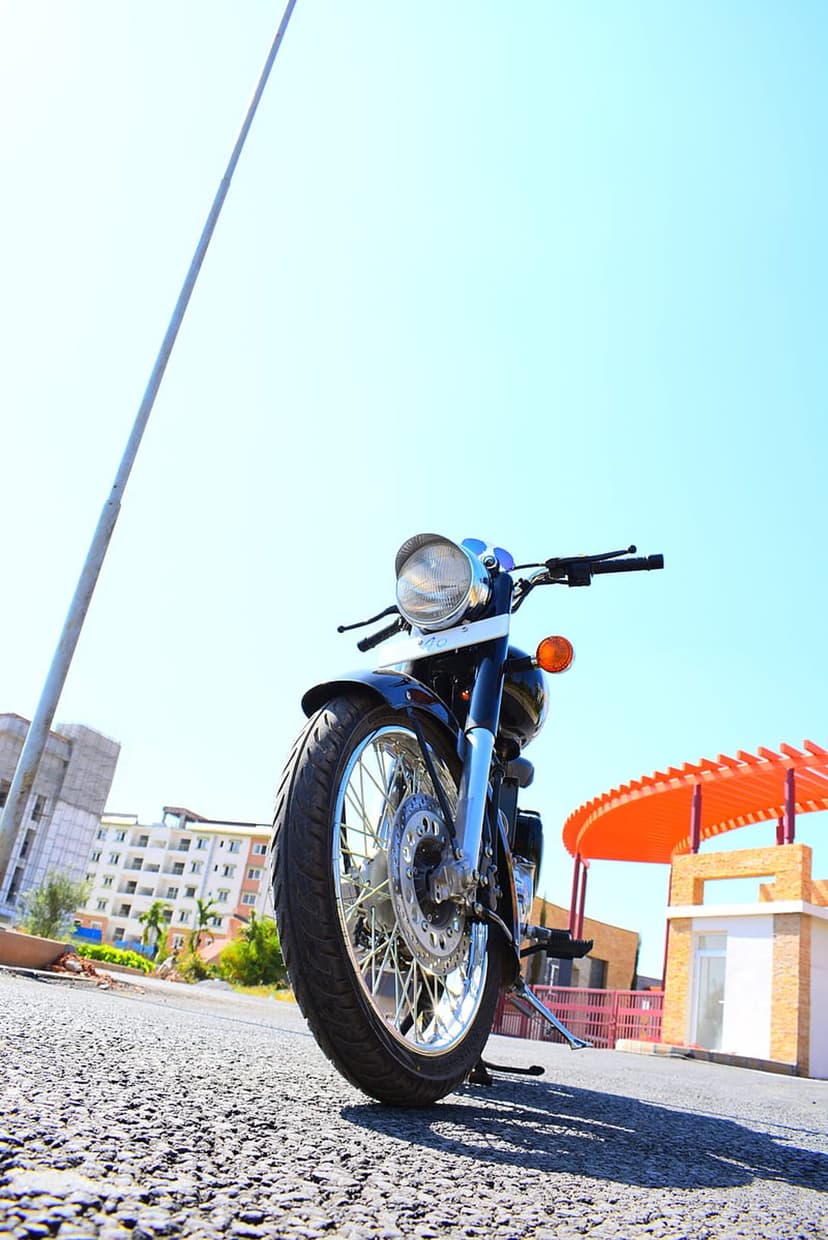 Black motorcycle front wheel and chrome headlight on asphalt under a clear blue sky with an orange building.
