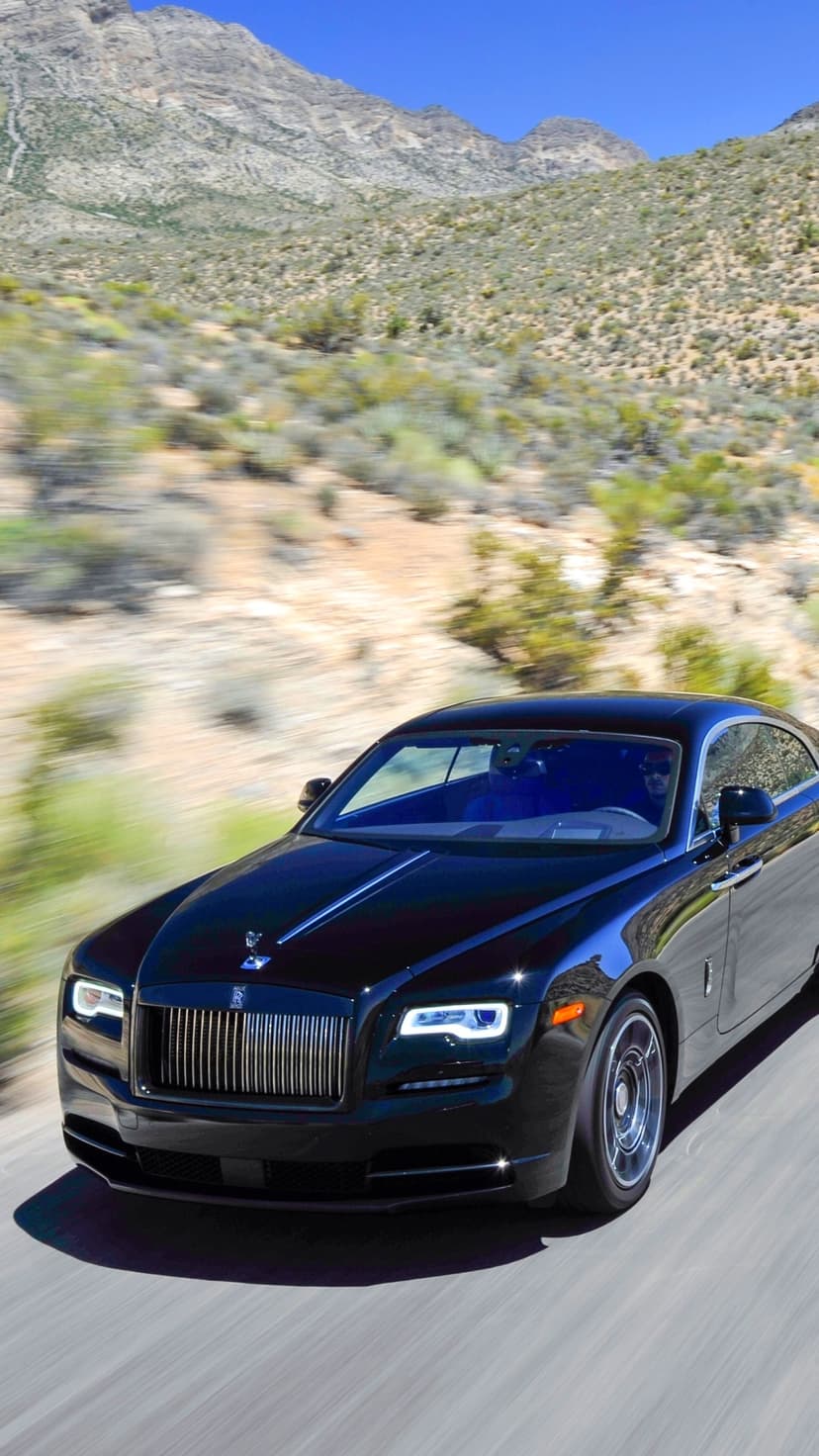 Black Rolls-Royce Wraith driving fast on a desert road with motion blurred arid mountains in the background.