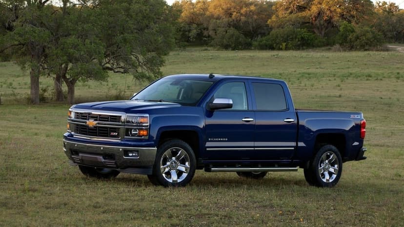 Blue Chevrolet Silverado Z71 pickup truck parked in a green field with trees in the background under soft light.