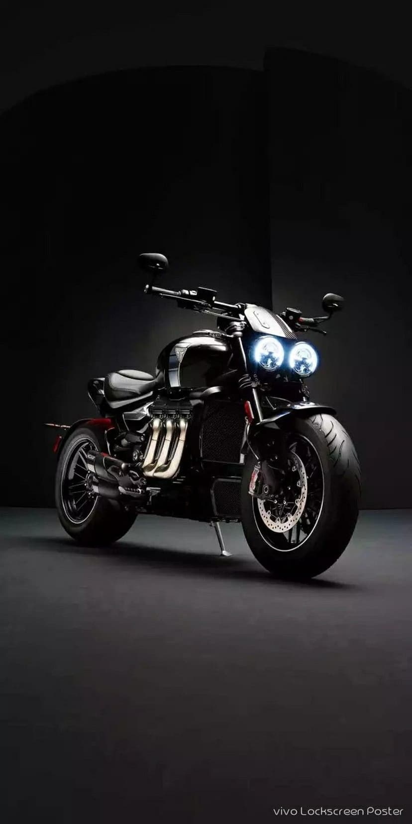 Triumph Rocket 3 motorcycle with dual circular LED headlights and chrome exhaust pipes against a dark backdrop.