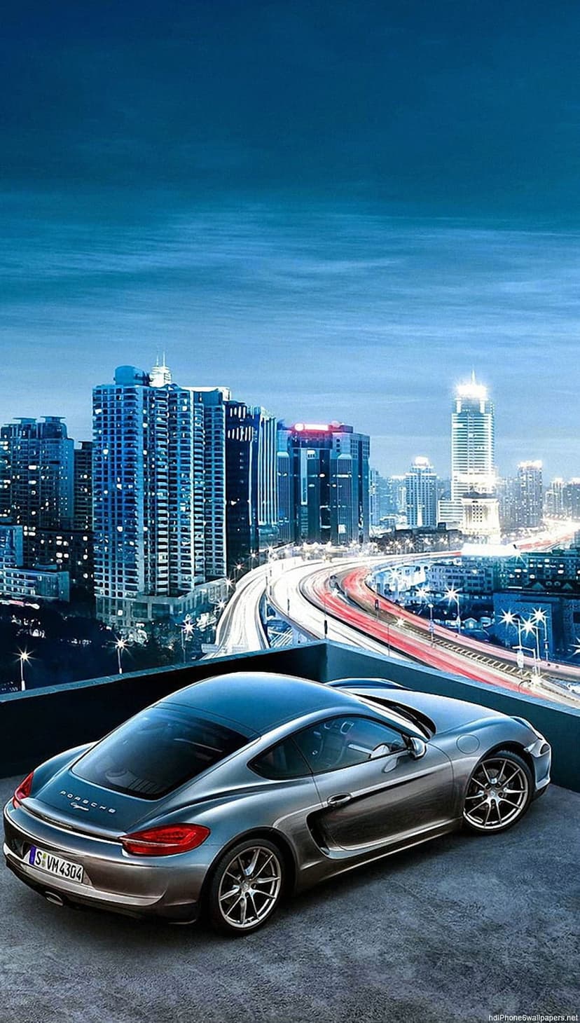 Silver Porsche sports car parked on a rooftop overlooking a glowing city skyline with highway light trails.