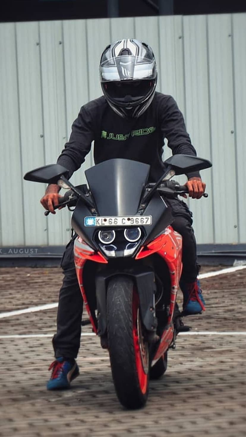 Biker wearing a silver helmet sits on an orange motorcycle featuring dual headlights and vibrant black frame.