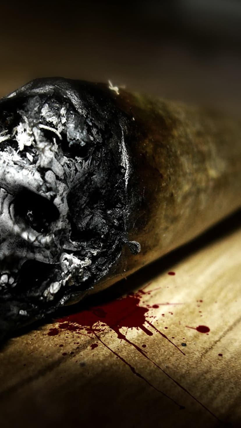 Burnt cigarette with skull-shaped ash lies near crimson blood splatters on a dark, textured wood surface.