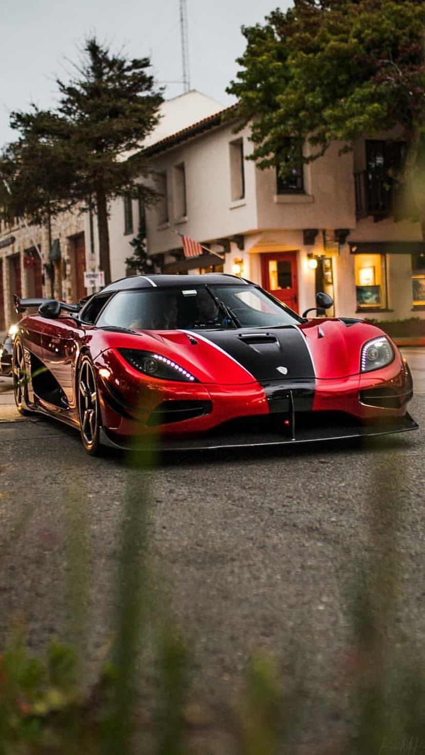 Koenigsegg Agera RS in red and black drives through a city at night with its bright LED headlights illuminated.