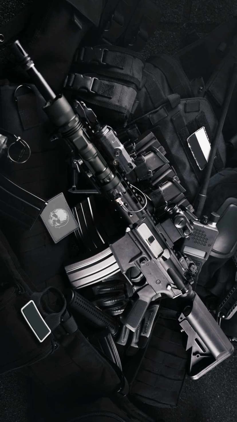 Tactical AR-15 rifle rests on a loadout vest with spare magazines and a radio in sharp monochrome contrast.