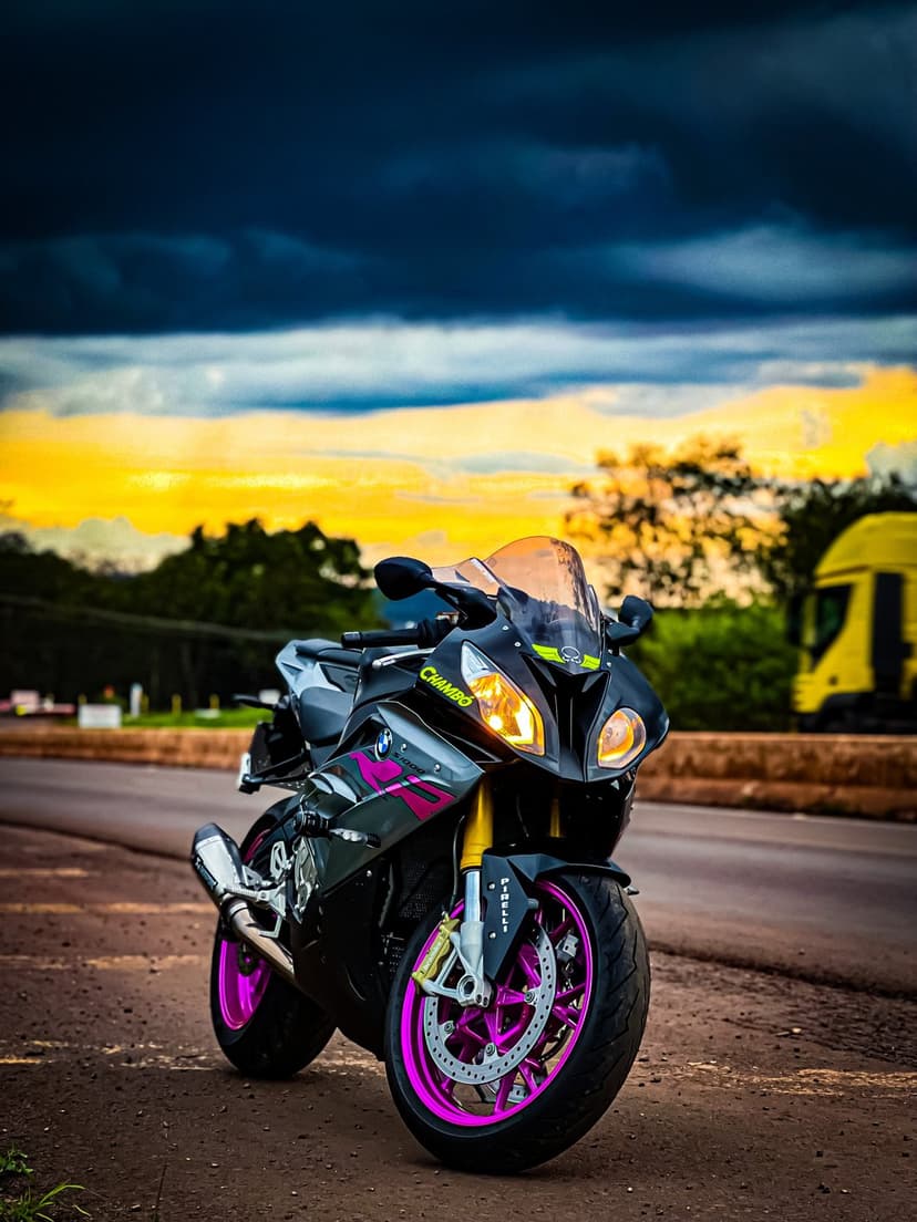 BMW S1000RR motorcycle with pink wheels parked on a dirt road during a dramatic yellow and gray storm sunset.