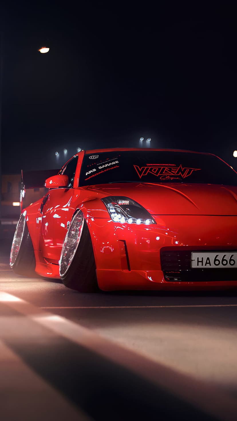 Crimson Nissan 350Z with wide body kit and cambered wheels parked at night showing a Violent decal on the glass.