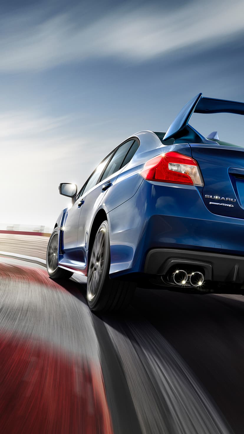 Blue Subaru WRX STI racing on a track with motion blur, low angle view of rear spoiler and exhaust.