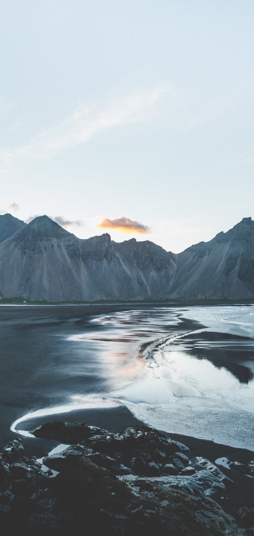 Volcanic black sand beach reflects a purple twilight sky and rugged mountain range during a receding tide.