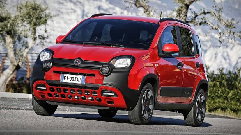 Red Fiat Panda Cross compact SUV on a road with trees and distant hills in soft daylight.