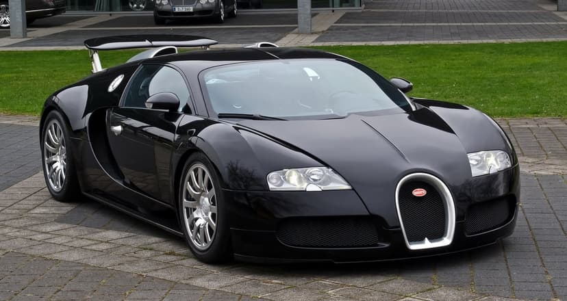 Black Bugatti Veyron with silver wheels parked on a stone driveway against a green grass background.