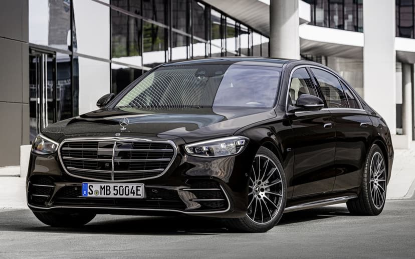 Black Mercedes-Benz S-Class sedan parked on pavement in front of a modern glass building with sleek reflections.