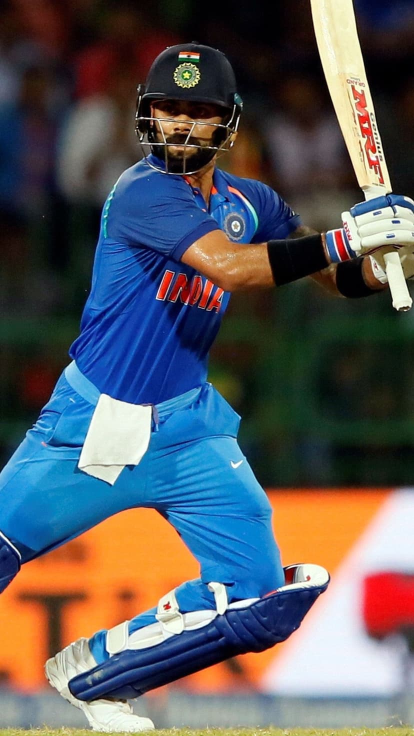 Virat Kohli wearing a blue Indian cricket uniform and helmet grips a bat while preparing for a match strike.