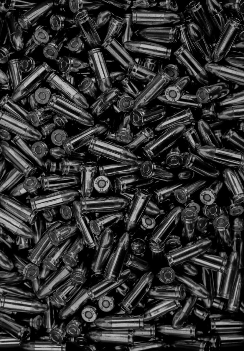Silver ammunition rounds piled together with metallic reflections on a dark, textured surface.