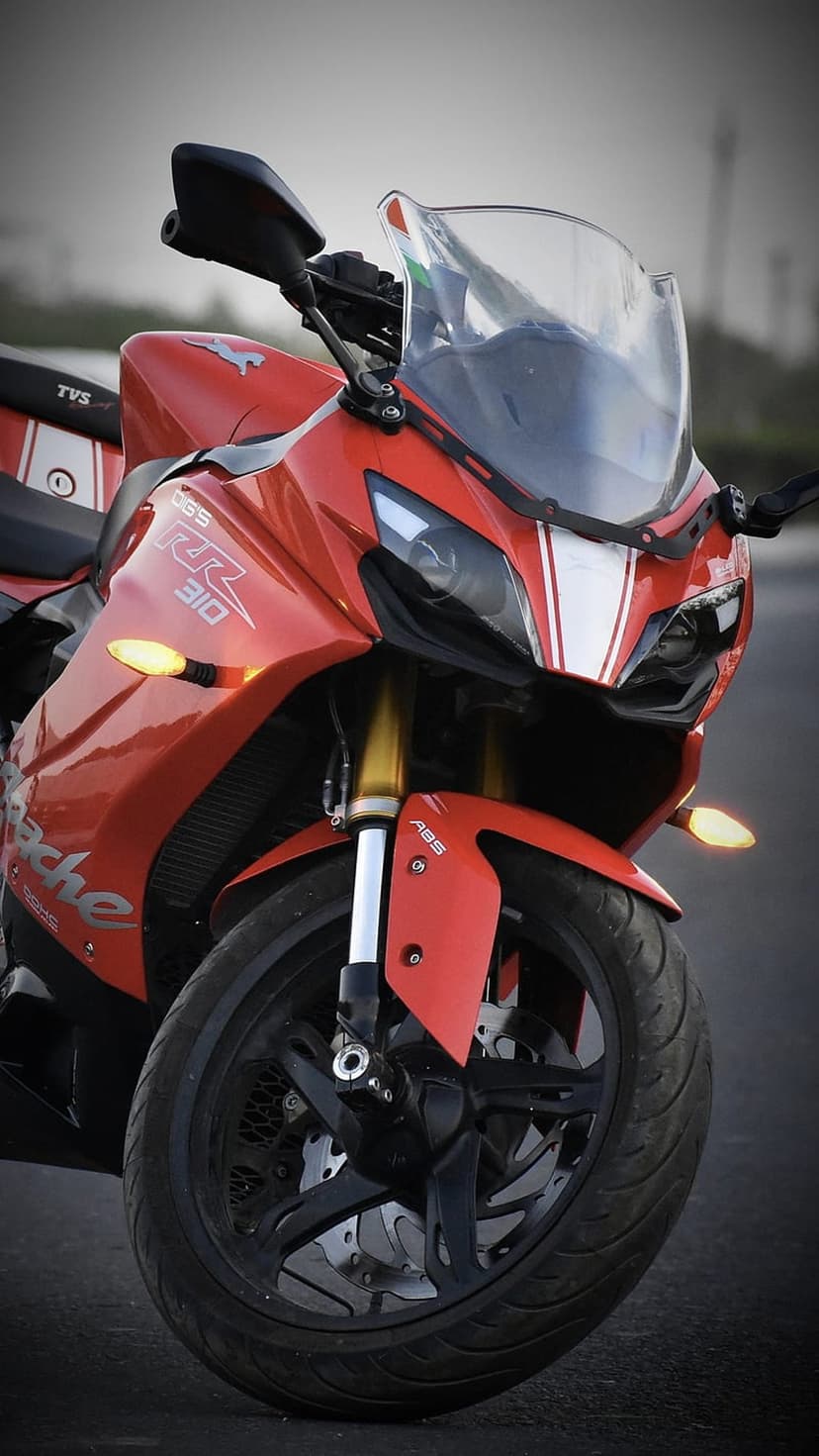 TVS Apache RR 310 motorcycle features a red fairing, twin LED headlights, and a front disc brake assembly.