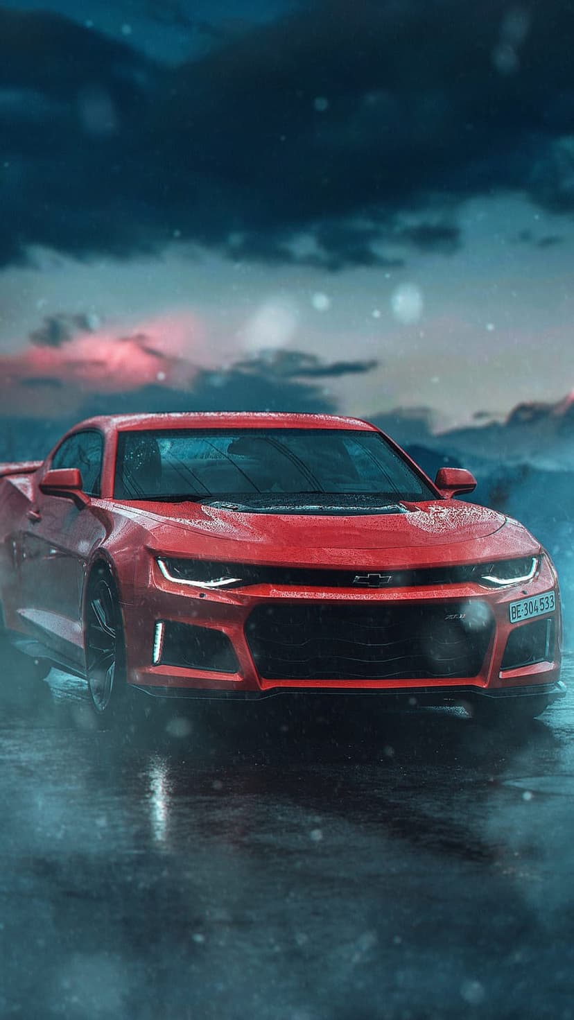 Crimson Chevrolet Camaro with glowing headlights sits on a wet road under a pink and blue snowy twilight sky.
