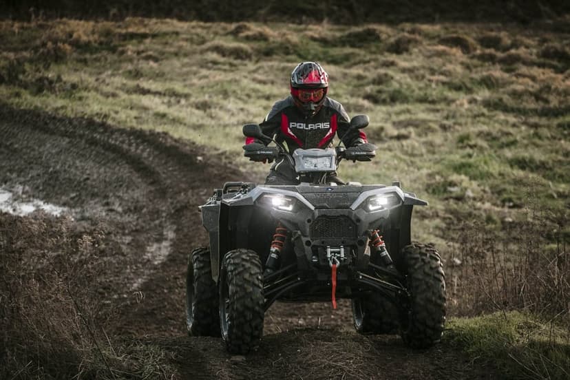 Rider on a Polaris ATV with headlights on driving through a muddy field on a cloudy day with high depth.