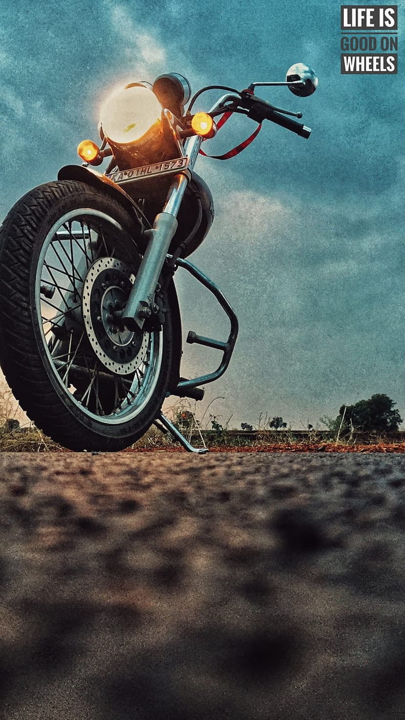 Royal Enfield motorcycle wheel and chrome headlight under a cloudy sky with life is good on wheels text overlay.