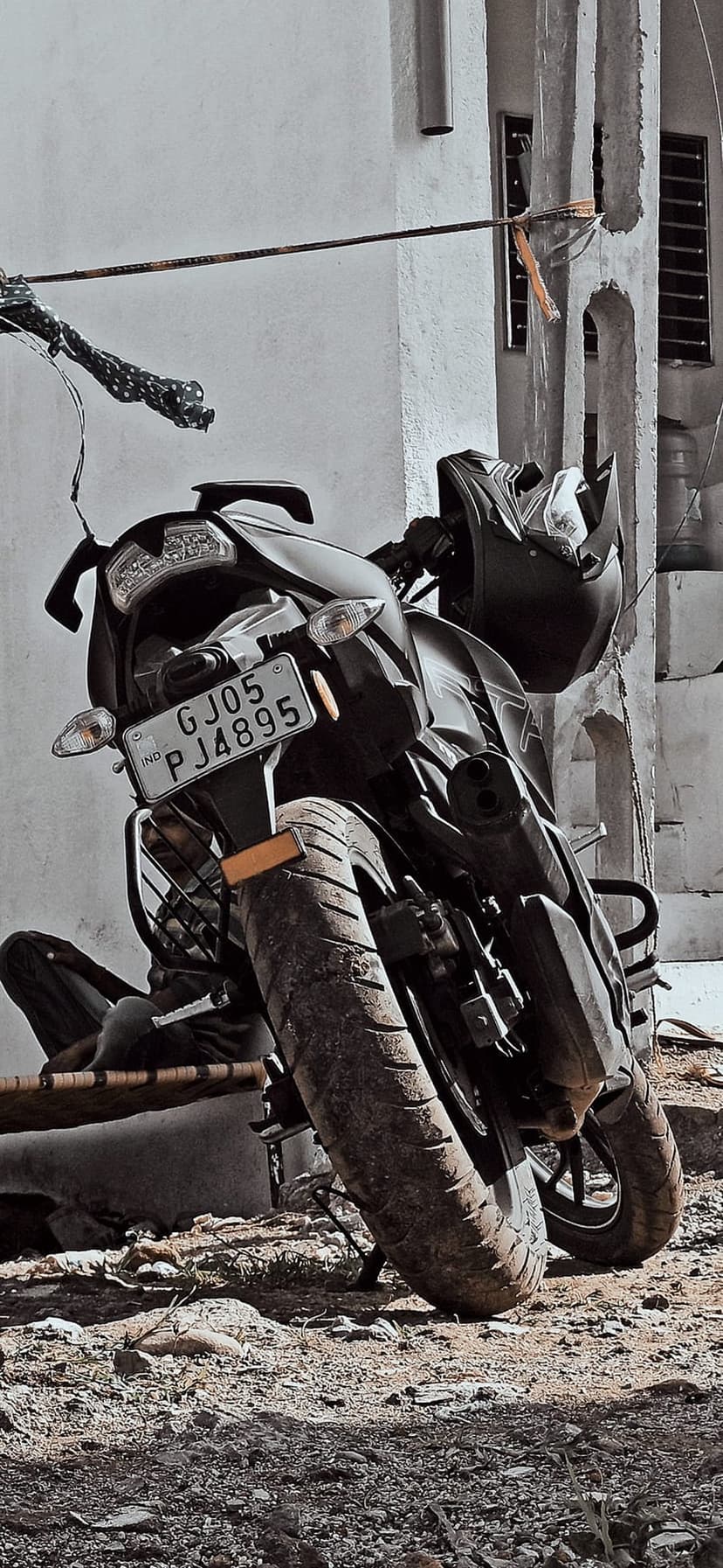 Black motorcycle with a helmet on the handlebars parked beside a textured building wall in monochrome.