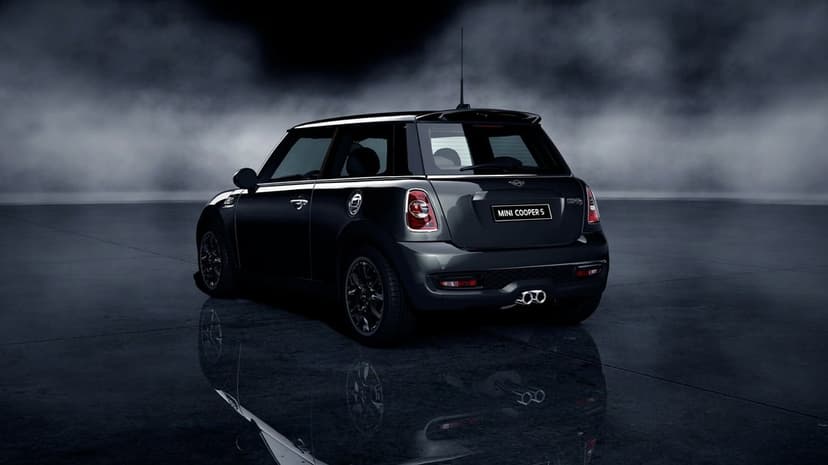 Rear view of a black Mini Cooper S on a reflective floor with smoke and mist in a dark studio setting.