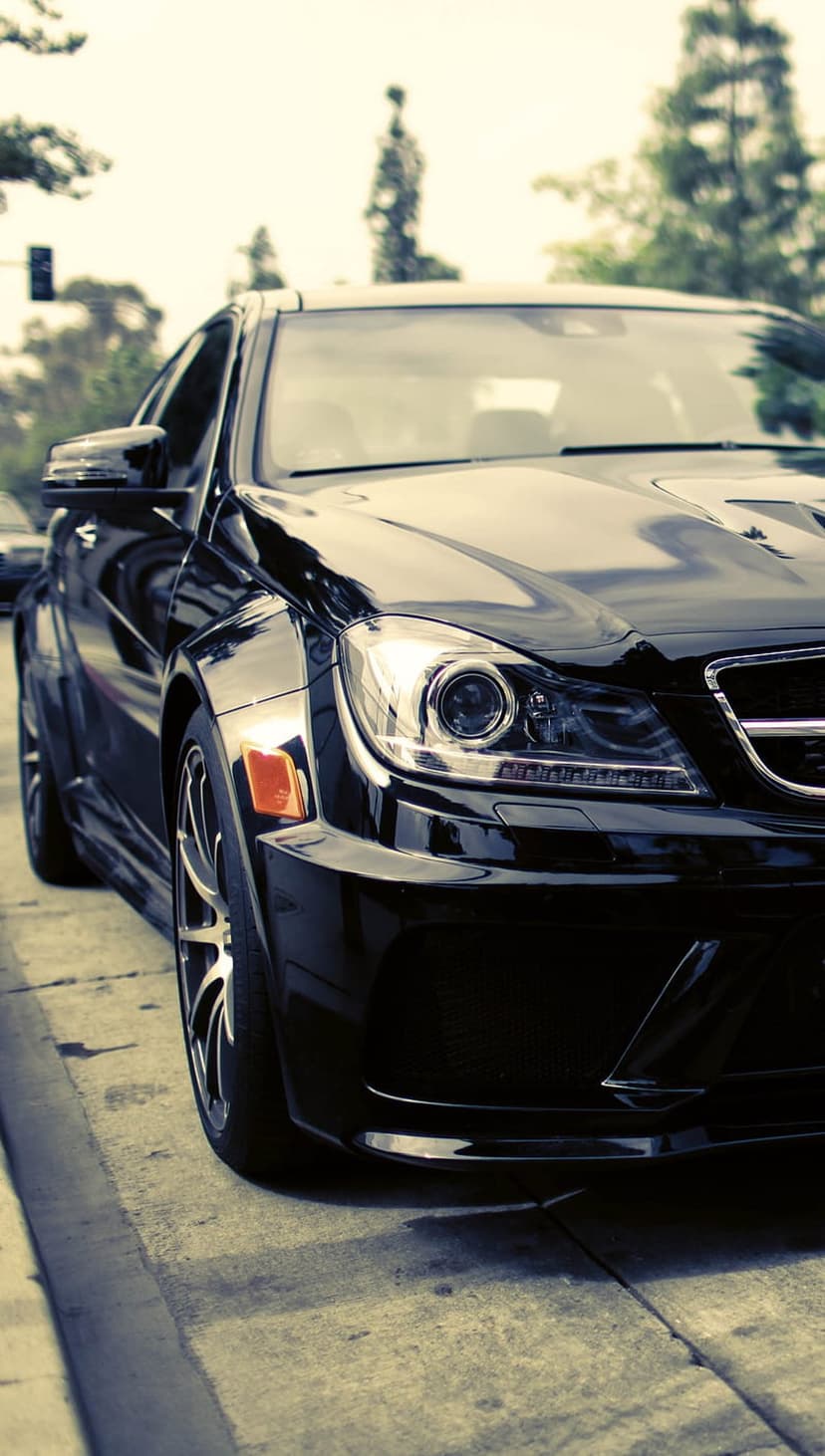 Black luxury sedan with chrome grilles and alloy wheels parked on a street under bright daylight reflections.