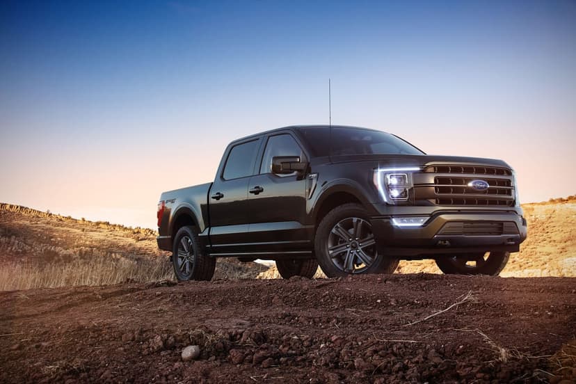Dark Ford F-150 truck with glowing LED lights parked on a rocky desert hill during a colorful sunset.