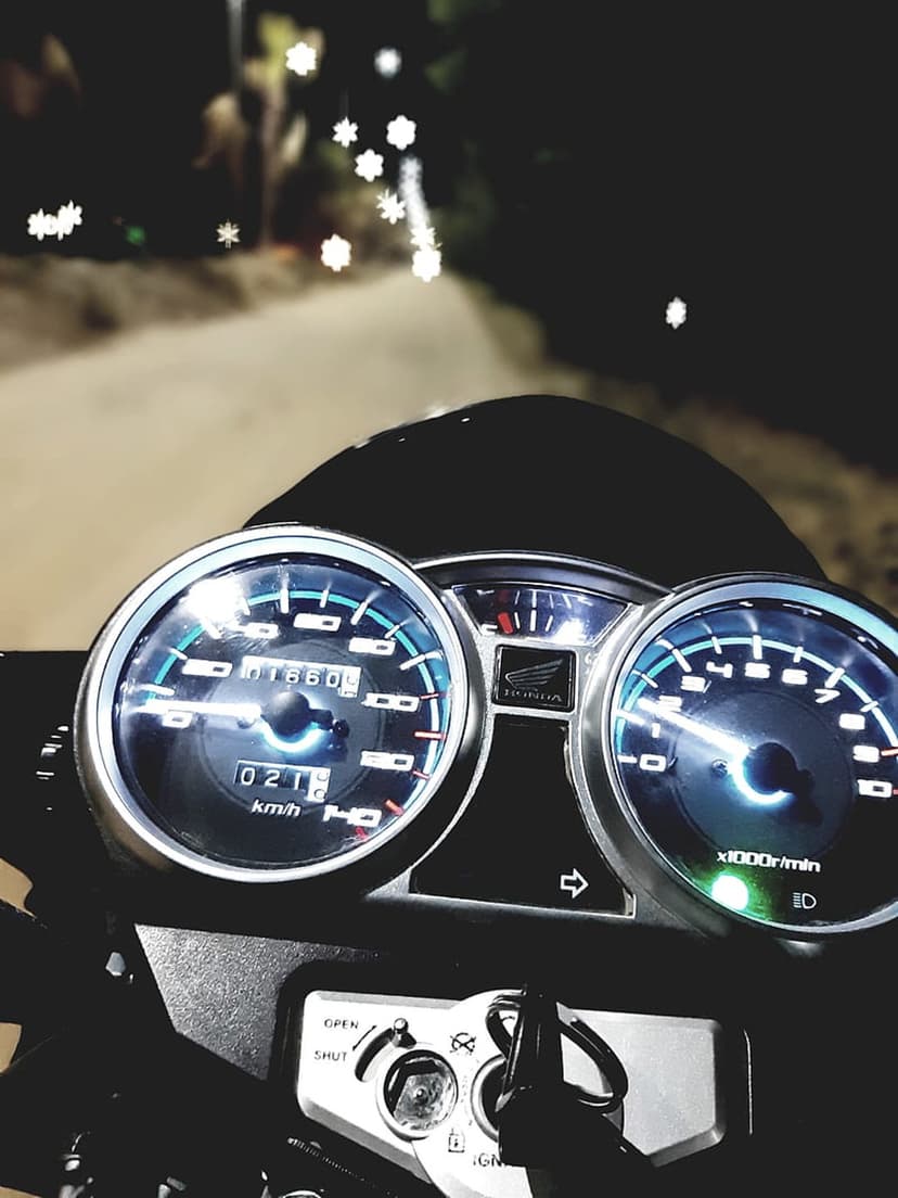 Motorcycle speedometer and tachometer glow with orange light against a blurred background of city night bokeh.