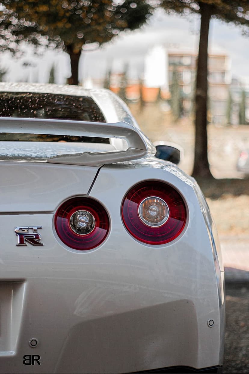 White Nissan GT-R rear view showing red circular taillights and a sporty spoiler against a blurred background.
