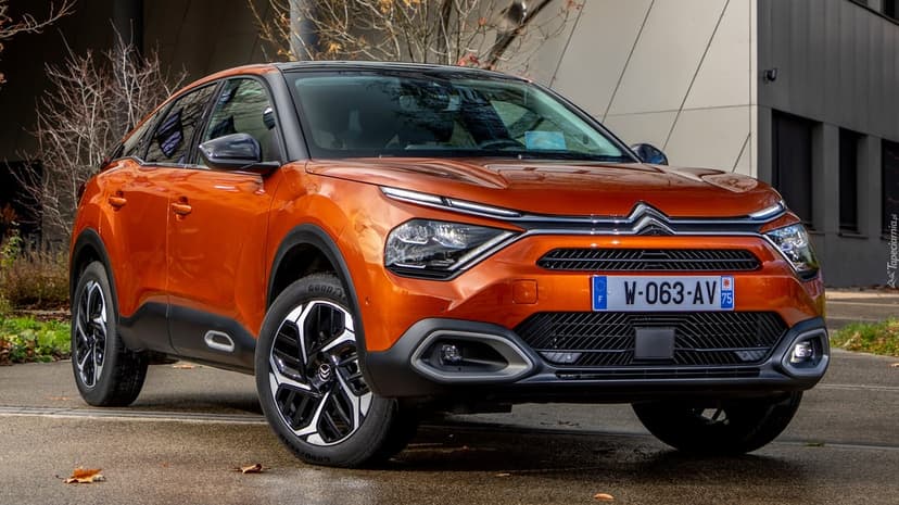 Orange Citroen C4 parked on a paved road in front of a modern building with a shallow depth of field.