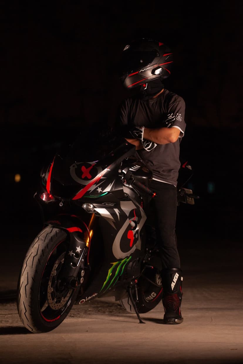 Motorcyclist in black racing leathers stands by a custom sport bike with red graphics under dark night lighting.