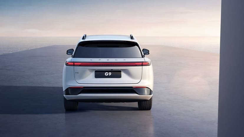White XPENG G9 SUV rear view on a concrete deck overlooking the ocean during a soft, hazy sunset.