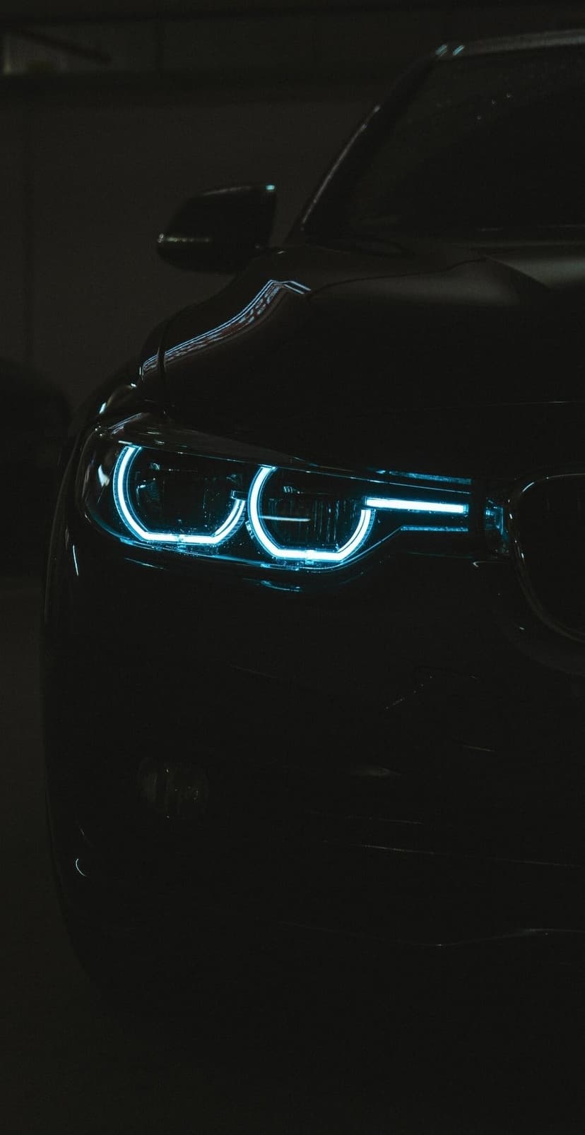 BMW twin circular headlights glow with electric blue LED rings against a dark, metallic front vehicle grille.