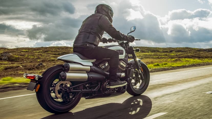 White Sportster S motorcycle cruising a scenic road under dramatic sunbeams and heavy clouds with a rider in black.